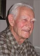 A smiling person with short white hair and a plaid shirt is looking to the side in an indoor setting with neutral-colored walls.